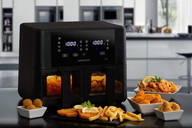 A Kenwood 9L dual modern airfryer with digital displays and viewing windows. The black appliance is surrounded by bowls of yellow and golden fried foods, including french fries, nuggets, and calamari